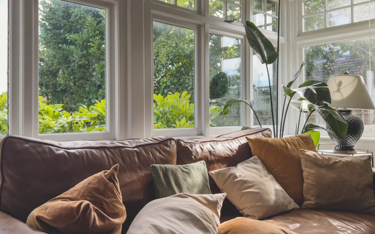 A,Brown,Leather,Sofa,With,Scattered,Pillows,,Typical,Windows,And